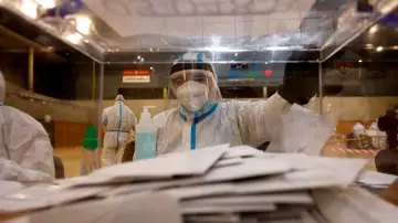 Una mujer equipada con equipos de protección individual (EPI) trabaja en una mesa electoral Una mujer equipada con equipos de protección individual (EPI) trabaja en una mesa electoral