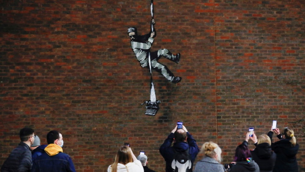 Un grupo de personas toma fotos del nuevo grafiti de Banksy de la prisión inglesa de Reading
