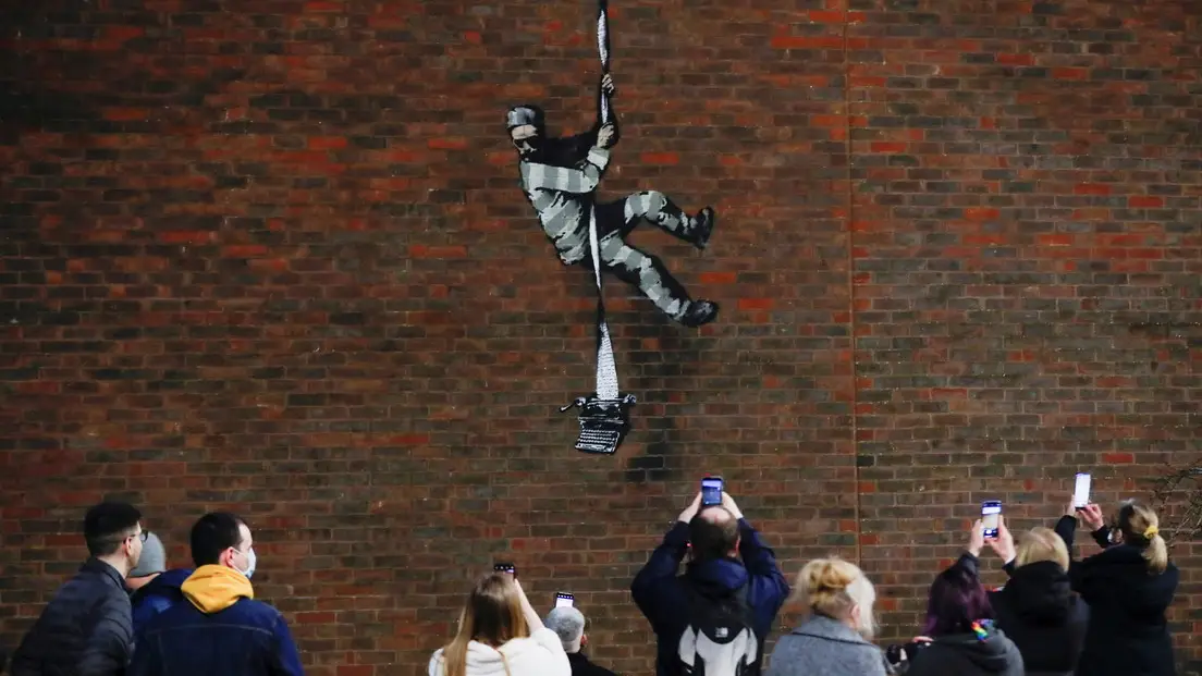 Un grupo de personas toma fotos del nuevo grafiti de Banksy de la prisi&oacute;n inglesa de Reading