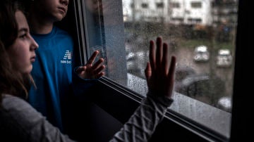 Emma (i) y Bruno (d), primos que se encuentran confinados juntos, a causa de que la madre de él trabaja como médico en la UCI de el Valle de Hebrón, en Barcelona, y ha debido tomar la decisión de confinar a su hijo en casa de unos familiares. Muchos trabajadores sanitarios han decidido autoconfinarse o aislarse para proteger a sus familias durante la primera oleada de la pandemia de coronavirus en España. La niña ese día cumple 11 años. Día de lluvia, la tercera semana de confinamiento domiciliario y estado de alarma. (© Xavier Bertral)