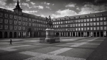 Una persona cruza la solitaria Plaza Mayor de Madrid el primer día del confinamiento. Las sombrillas recogidas son el único recuerdo de las bulliciosas terrazas. Madrid, 15 de marzo, 2020. (© Carmenchu Alemán)