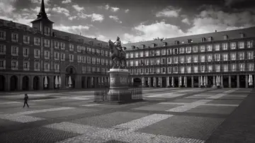 Una persona cruza la solitaria Plaza Mayor de Madrid el primer día del confinamiento. Las sombrillas recogidas son el único recuerdo de las bulliciosas terrazas. Madrid, 15 de marzo, 2020. (© Carmenchu Alemán)