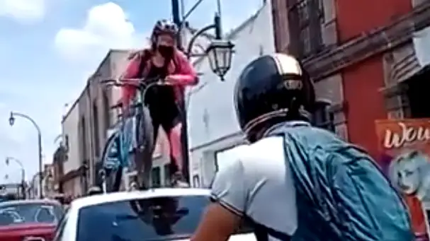 Una ciclista pasa con su bici por encima de un coche que estaba aparcado en un carril bici