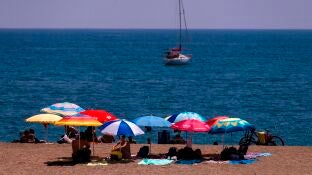 Unos ba&ntilde;istas se protegen del sol bajo las sombrillas en la playa de La Malagueta