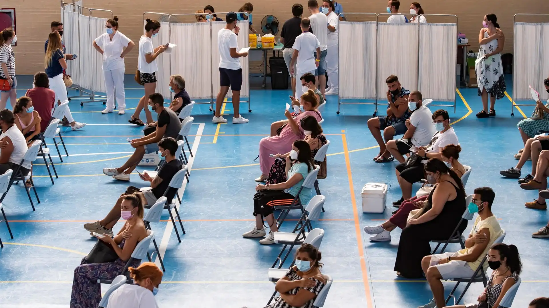 Multitud de jóvenes aguardan sentados tras recibir la vacuna contra el coronavirus en el pabellón municipal de Espartinas (Sevilla). Multitud de jóvenes aguardan sentados tras recibir la vacuna contra el coronavirus en el pabellón municipal de Espartinas (Sevilla).