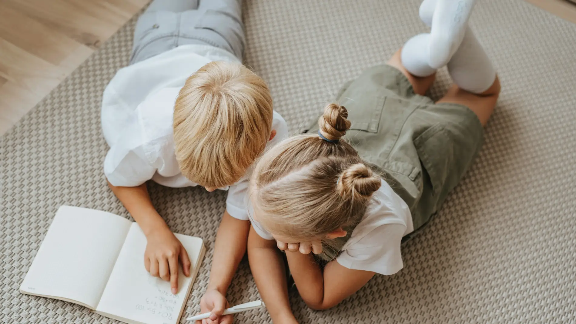 Niño y niña tumbados con una libreta.