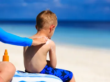 Un niño se deja poner la crema solar en la playa. Un niño se deja poner la crema solar en la playa.