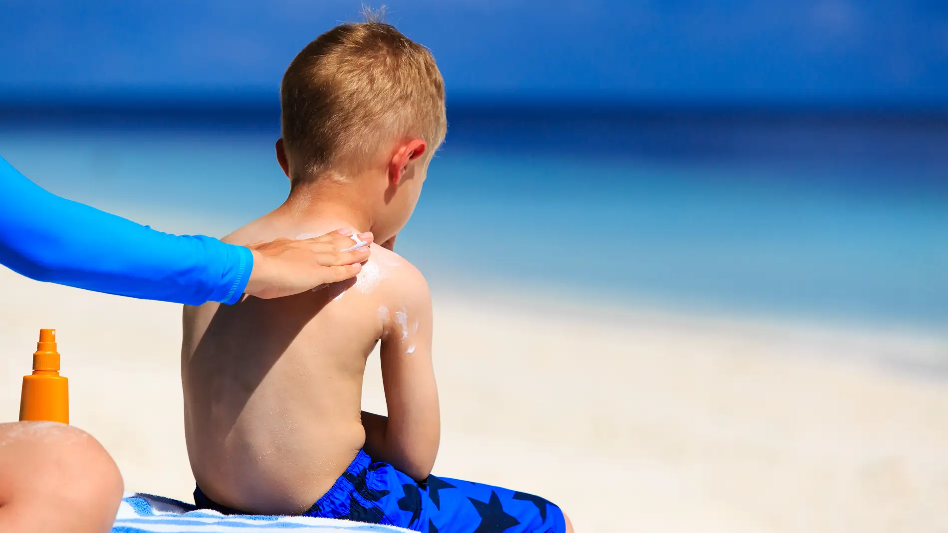 Un niño se deja poner la crema solar en la playa.