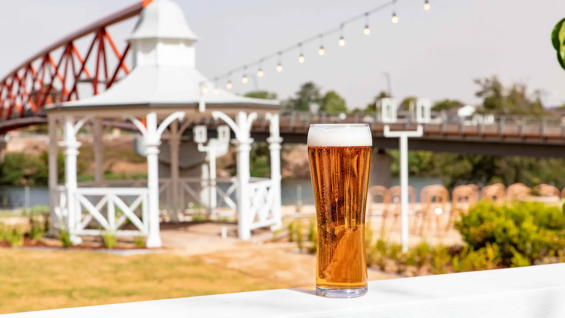 Copa de cerveza sobre una mesa. Al fondo vistas de una glorieta y un puente sobre un río
