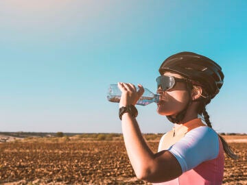 Una mujer en bicicleta bebe aguua para hidratarse.
