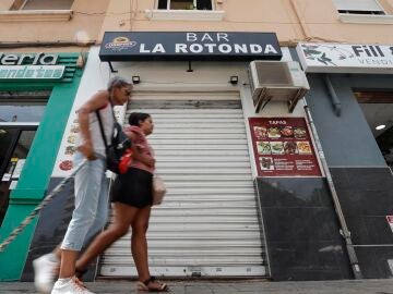 Dos mujeres pasan por delante de la persiana del bar, en Valencia