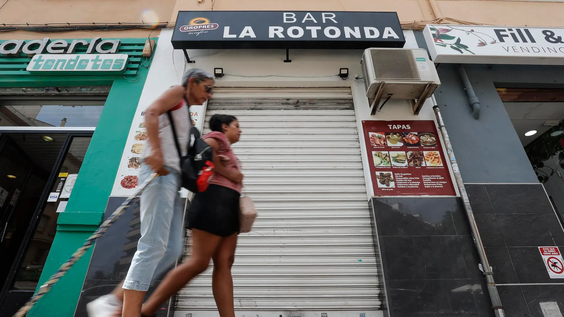 Dos mujeres pasan por delante de la persiana del bar, en Valencia Dos mujeres pasan por delante de la persiana del bar, en Valencia