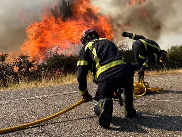 Efectivos de bomberos trabajan este domingo en la extinción de un incendio forestal en la carretera N120, actualmente cortada por las llamas, en A Cañiza (Pontevedra)