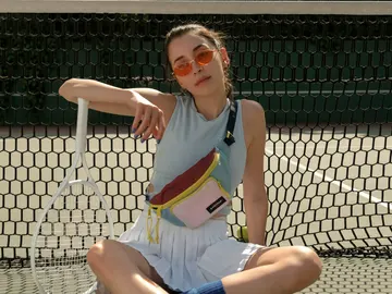 Chica con gafas de sol, riñonera, camiseta sin mangas, minifalda plisada, calcetines altos y deportivas en una pista de tenis. Chica con gafas de sol, riñonera, camiseta sin mangas, minifalda plisada, calcetines altos y deportivas en una pista de tenis.