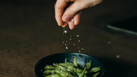 Por qué es importante consumir la sal yodada Mano añade sal a plato de verduras