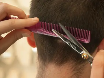 Un peluquero corta el pelo a un joven Un peluquero corta el pelo a un joven