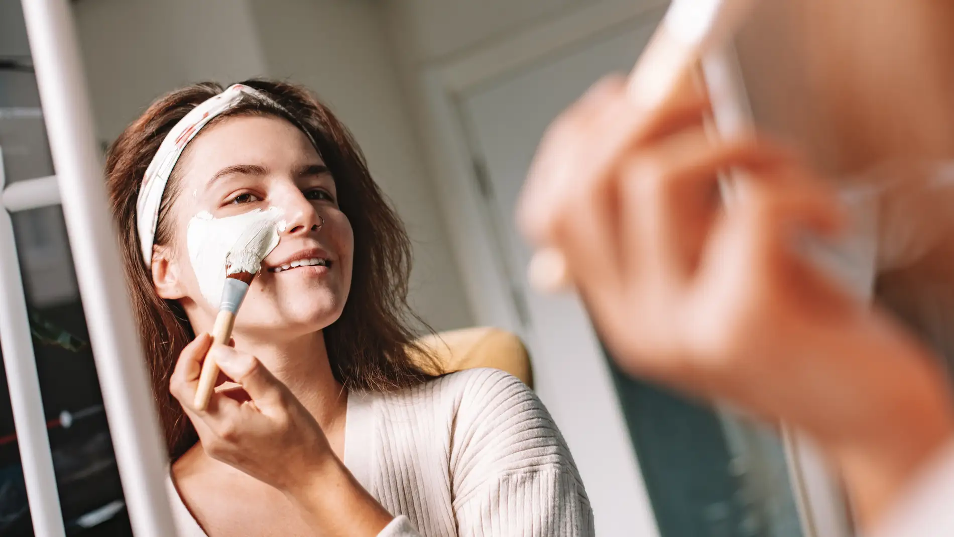 Mujer aplicándose un tratamiento facial con una brocha.