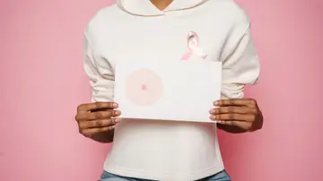Mujer que sostiene entre las manos un dibujo de un pecho mientras luce un lazo contra el cáncer de mama.