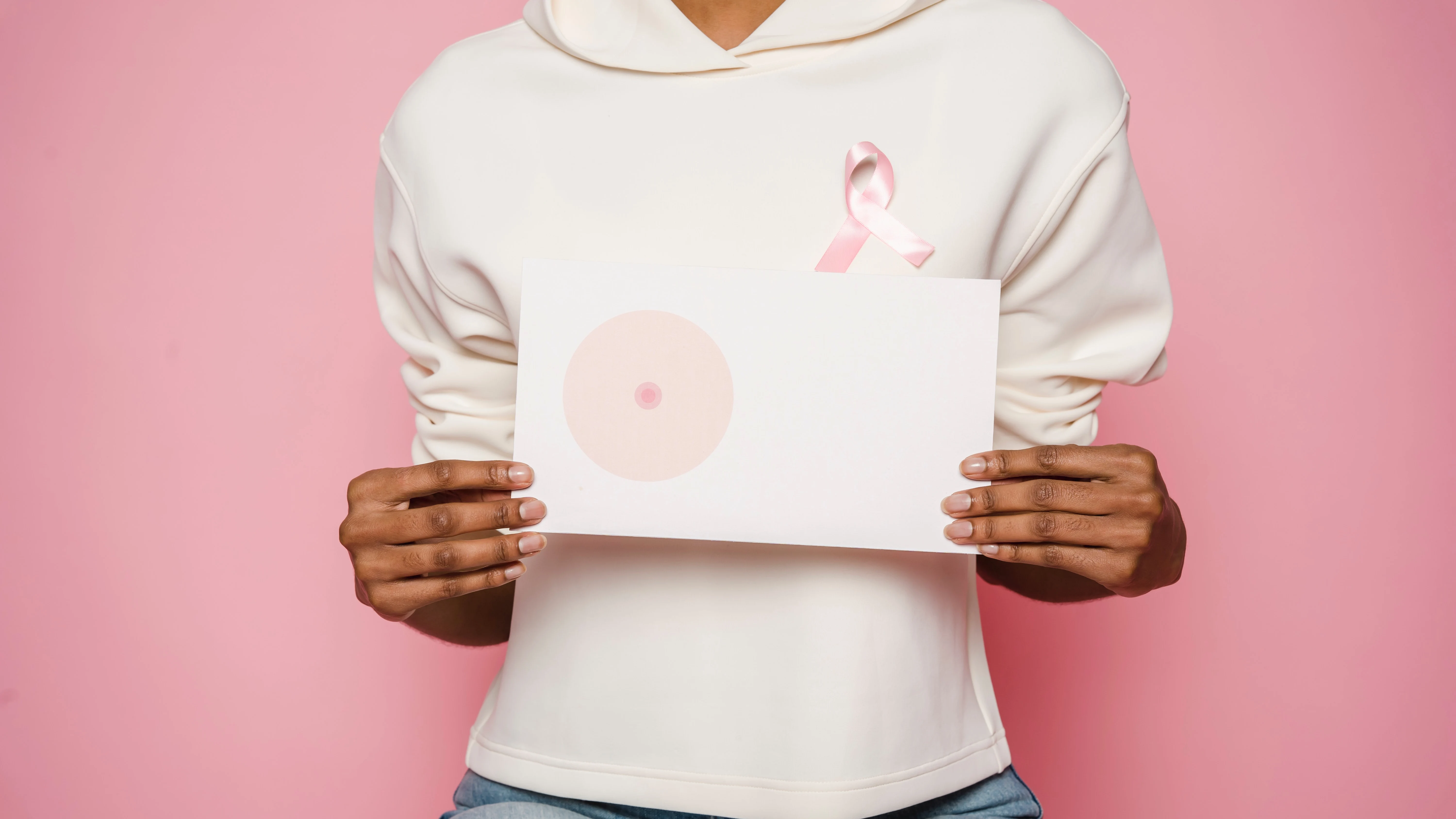 Mujer que sostiene entre las manos un dibujo de un pecho mientras luce un lazo contra el cáncer de mama. Mujer que sostiene entre las manos un dibujo de un pecho mientras luce un lazo contra el cáncer de mama.