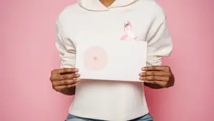 Mujer que sostiene entre las manos un dibujo de un pecho mientras luce un lazo contra el cáncer de mama.