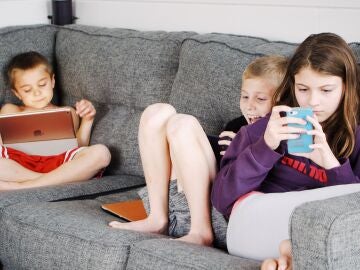 Tres niños en el sofá mirando la tablet y el teléfono móvil.