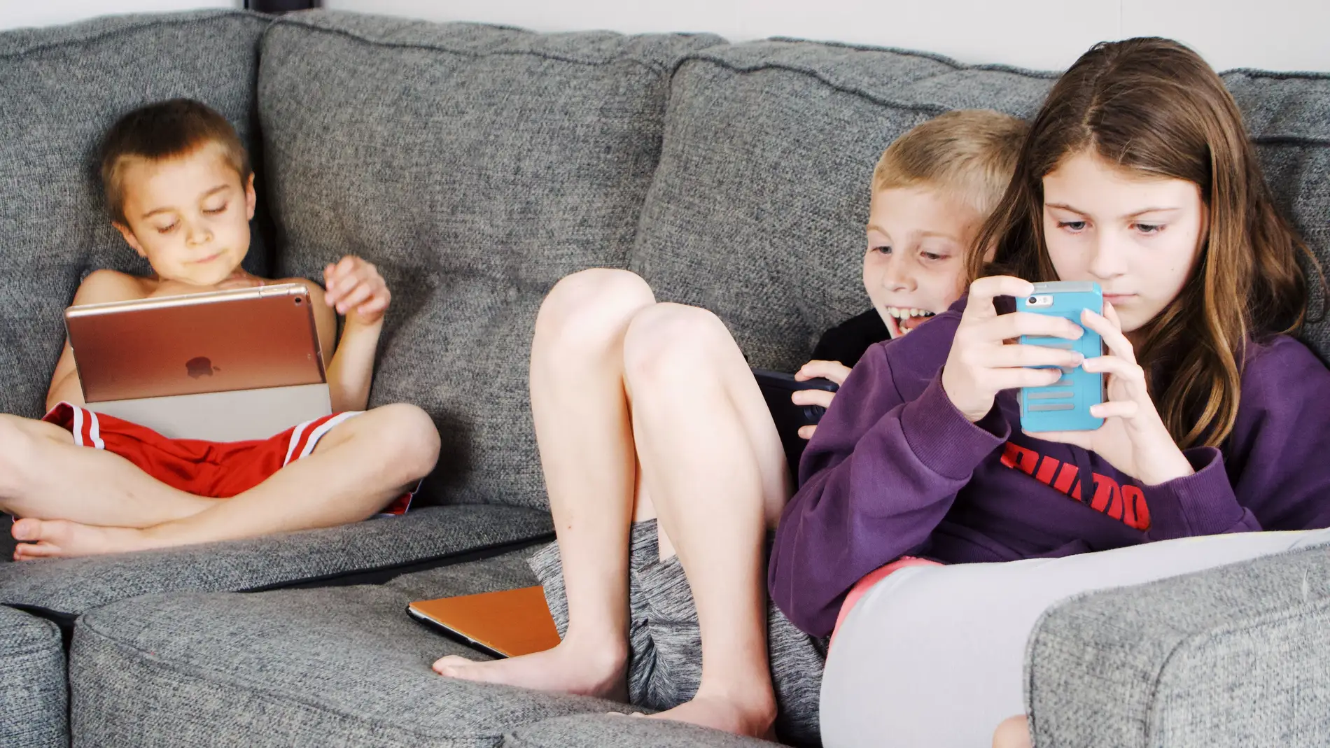 Tres niños en el sofá mirando la tablet y el teléfono móvil.