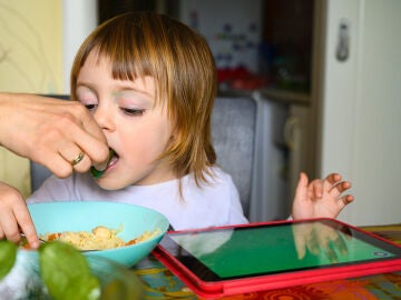 Un niño come mientras usa la tablet.