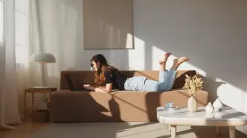 Una mujer tumbada en el sofá con el ordenador portátil