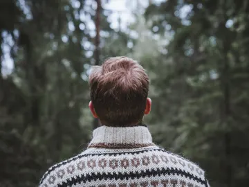 Hombre mirando el bosque de espaldas con un jersey con motivos navideños Hombre mirando el bosque de espaldas con un jersey con motivos navideños