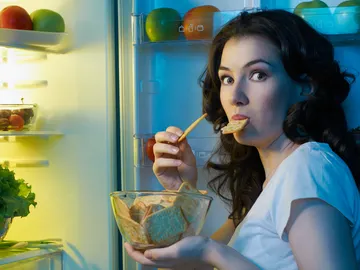Mujer comiendo frente a la nevera Mujer comiendo frente a la nevera