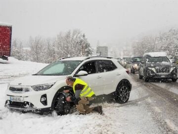 Imagen de recurso de un hombre colocando las cadenas a su coche en la nieve