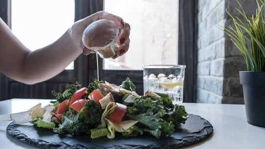 Primer plano de mano echando vinagreta a una ensalada