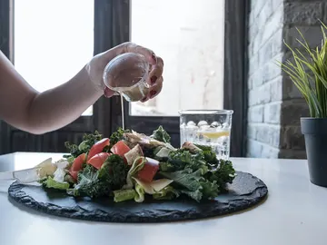Primer plano de mano echando vinagreta a una ensalada Primer plano de mano echando vinagreta a una ensalada