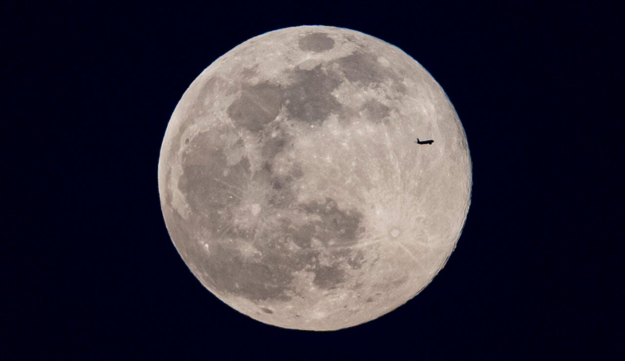 Un avión pasa por delante de la luna llena, este domingo en Madrid. Es la denominada luna llena de nieve.