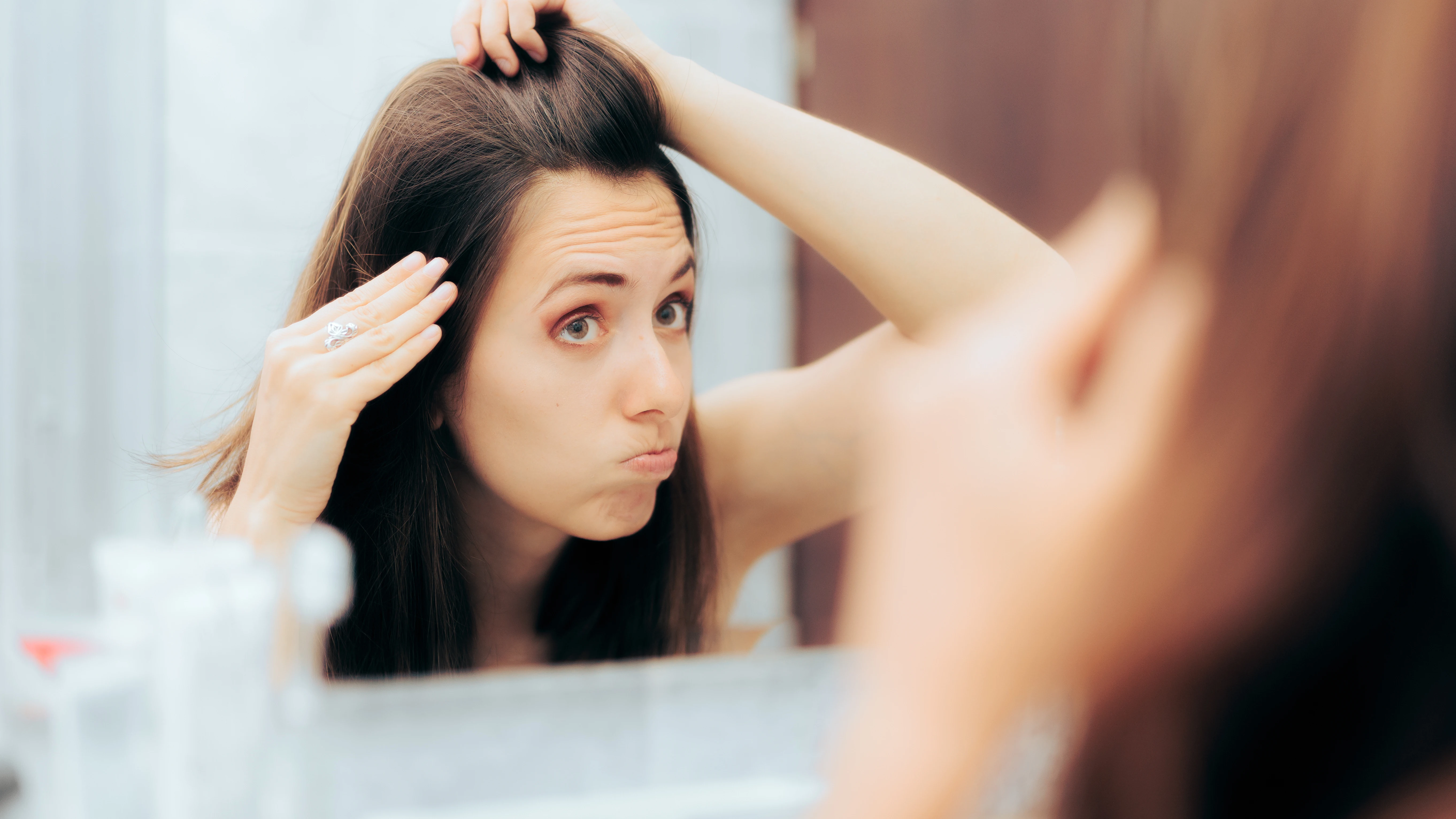 Chica mirándose el pelo en el espejo haciendo una mueca Chica mirándose el pelo en el espejo haciendo una mueca