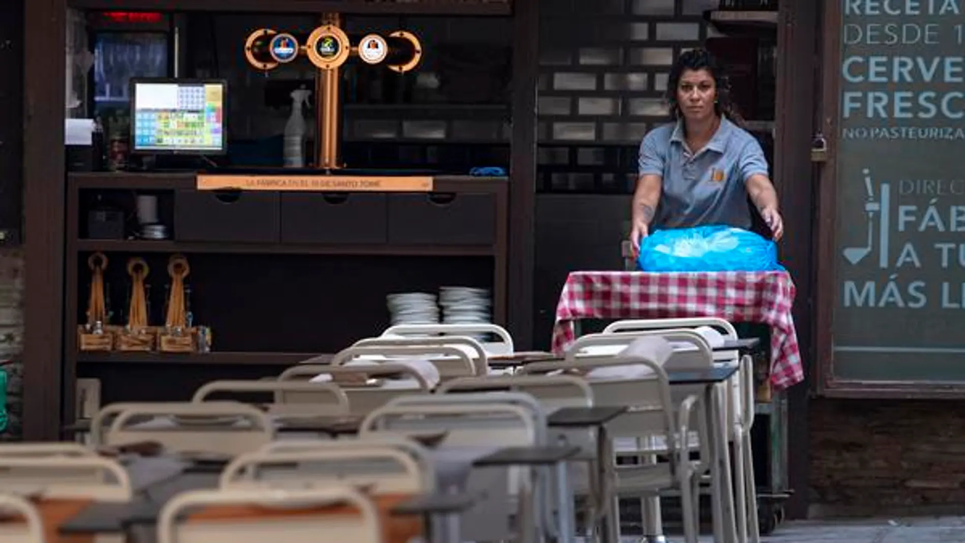 Una camarera coloca las mesa en un bar
