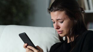 Una joven llorando al mirar el m&oacute;vil