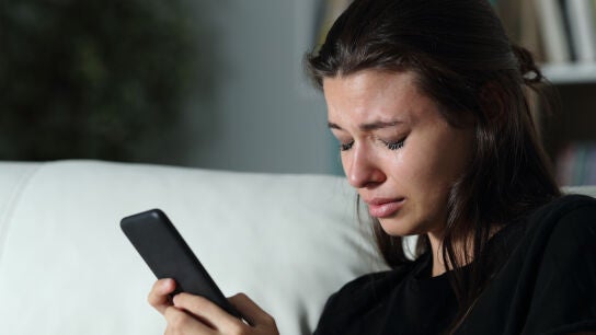 Una joven llorando al mirar el m&oacute;vil