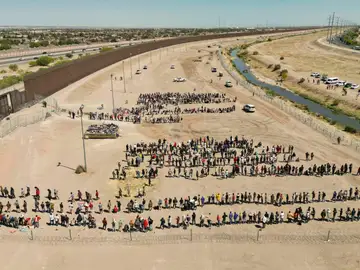 Migrantes mientras esperan junto al muro fronterizo en El Paso Migrantes mientras esperan junto al muro fronterizo en El Paso