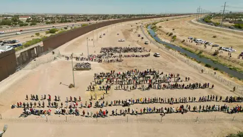 Migrantes mientras esperan junto al muro fronterizo en El Paso Migrantes mientras esperan junto al muro fronterizo en El Paso