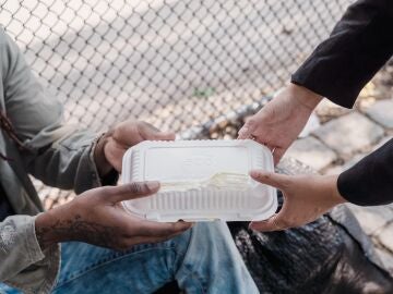 Persona dando comida a un indigente en la calle