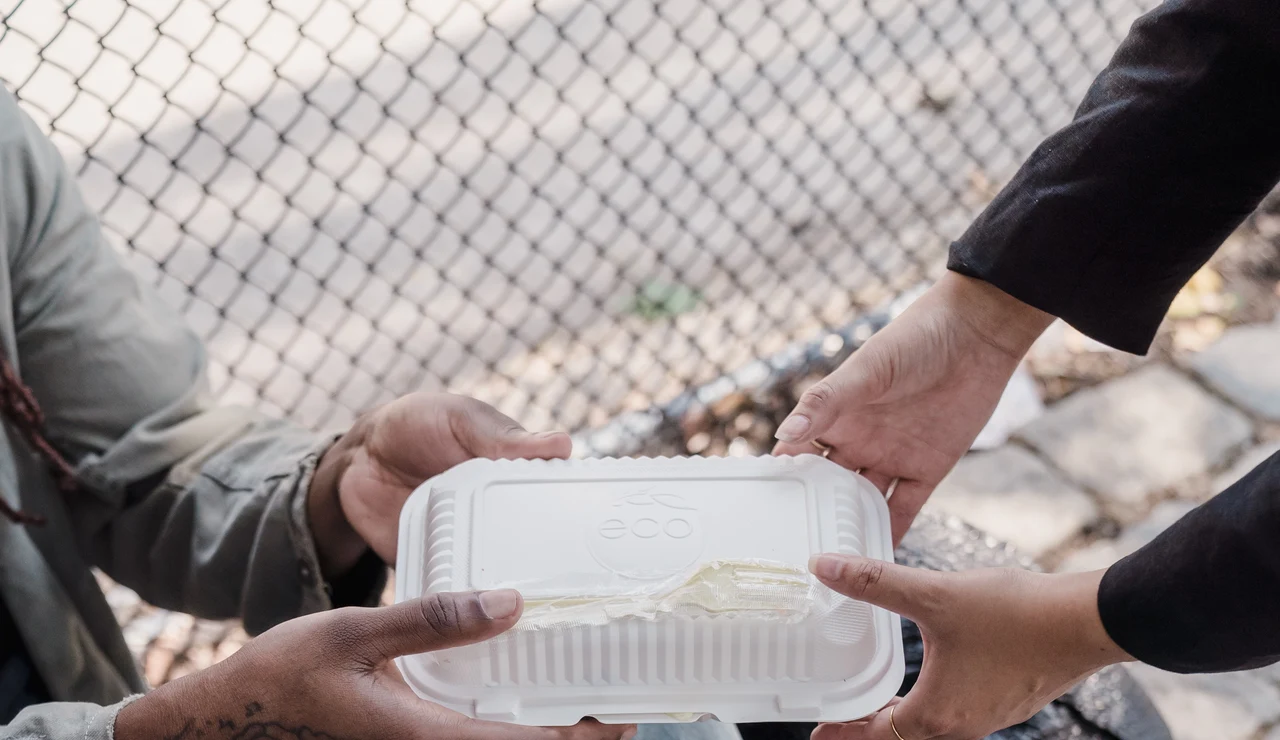 Persona dando comida a un indigente en la calle