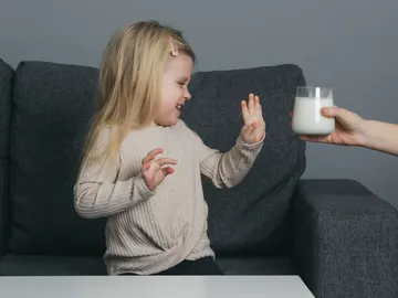 Una niña rechaza un vaso de leche Una niña rechaza un vaso de leche