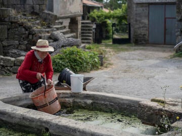 Una mujer llenando un cubo de agua en una fuente