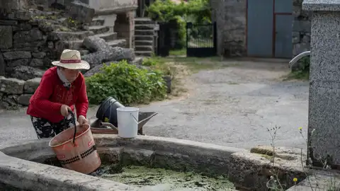 Una mujer llenando un cubo de agua en una fuente