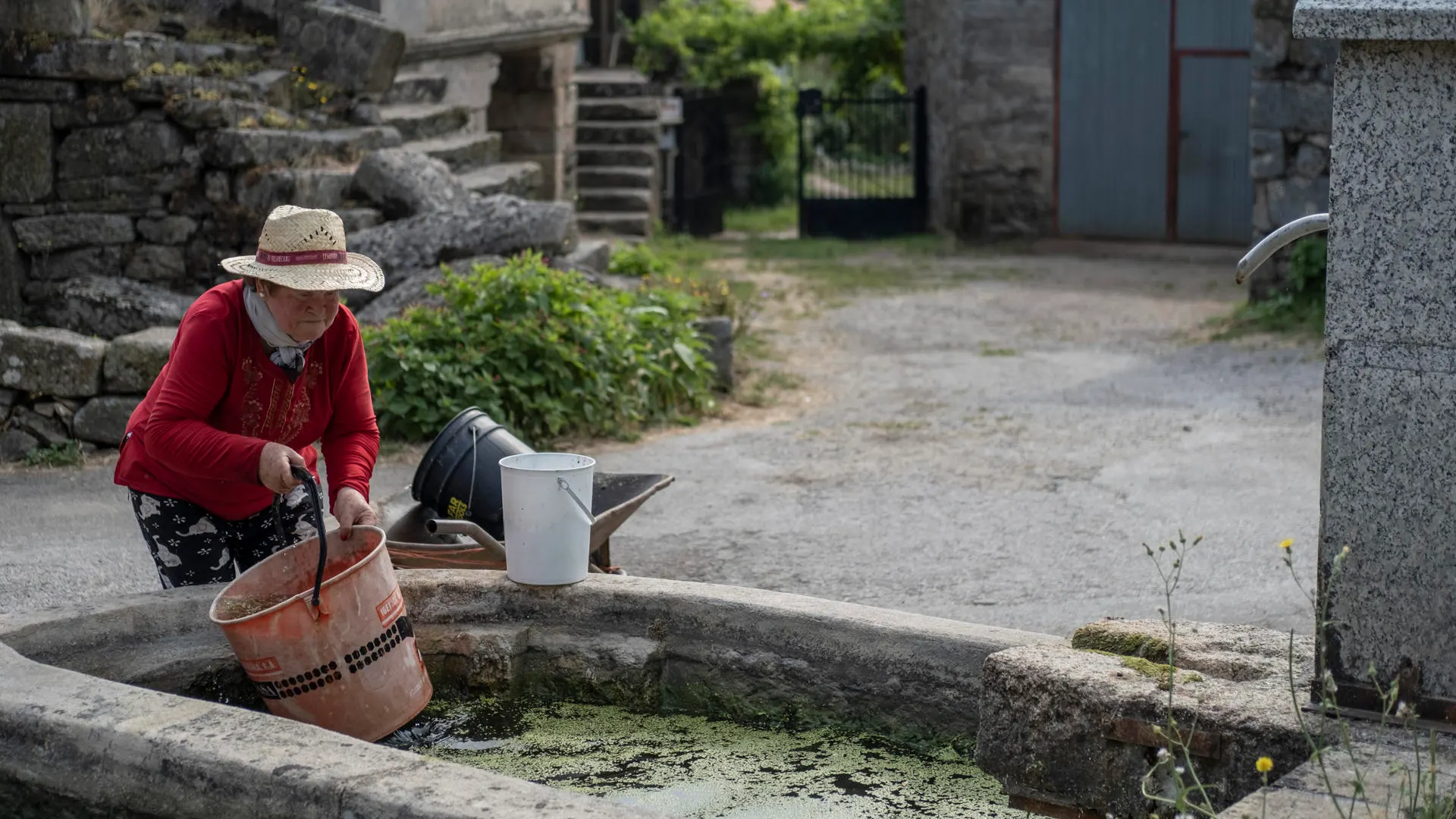 Una mujer llenando un cubo de agua en una fuente Una mujer llenando un cubo de agua en una fuente