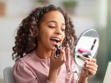 Niña pintándose los labios mientras se mira al espejo Niña pintándose los labios mientras se mira al espejo