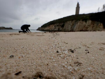 Una persona recoge pellets en la playa de As Lapas