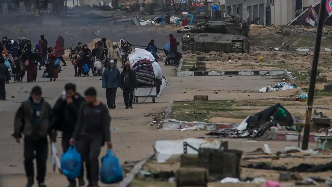 Los palestinos desplazados internos pasan junto a los tanques israel&iacute;es