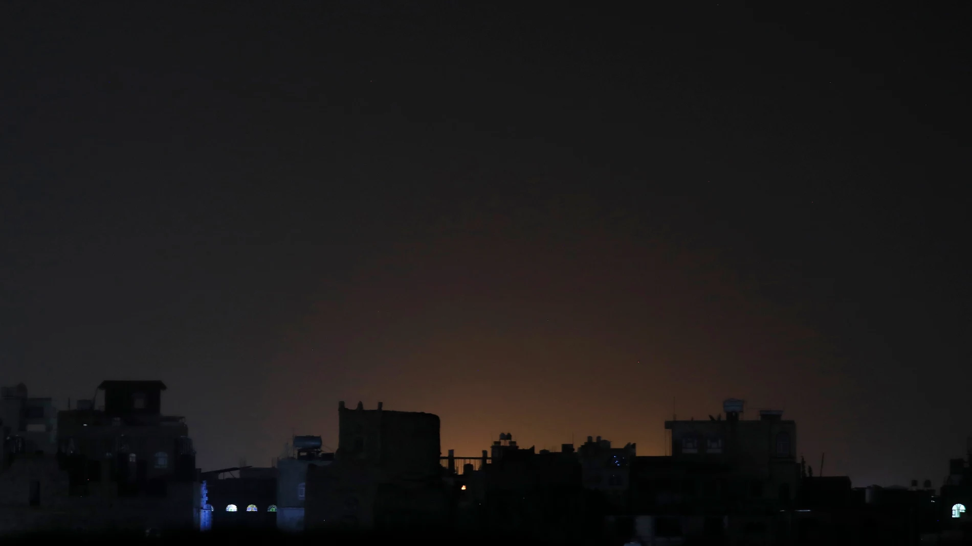 Vista general este sábado, 3 de febrero, del resplandor producto de ataques aéreos, detrás de un conjunto de edificios, en Saná